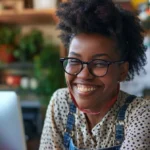 A woman with glasses smiles at the camera while using her laptop, representing an eFax alternative.